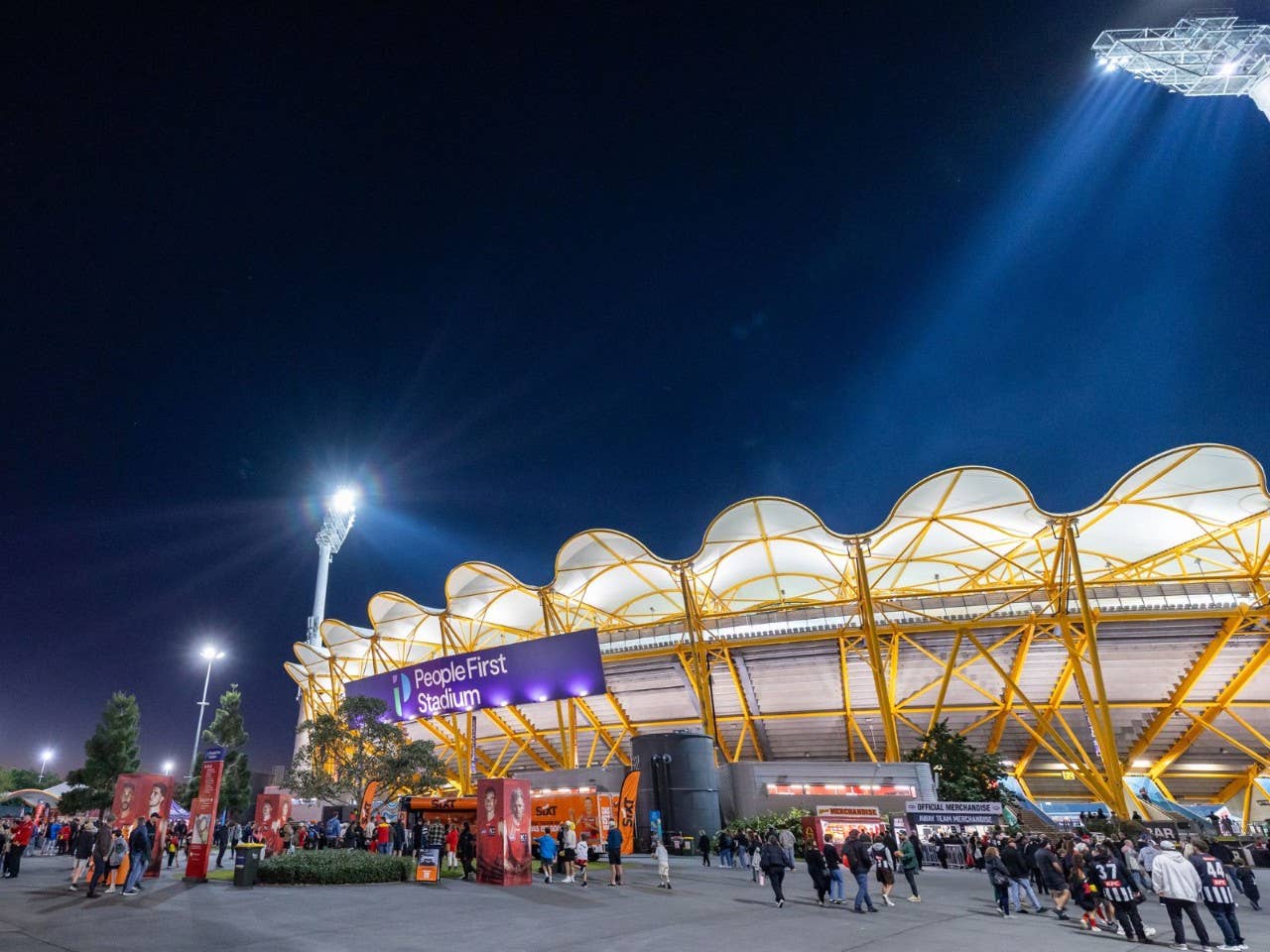 Night exterior of People First Stadium with illuminated signage and roof structure, as patrons gather outside the venue before a match.